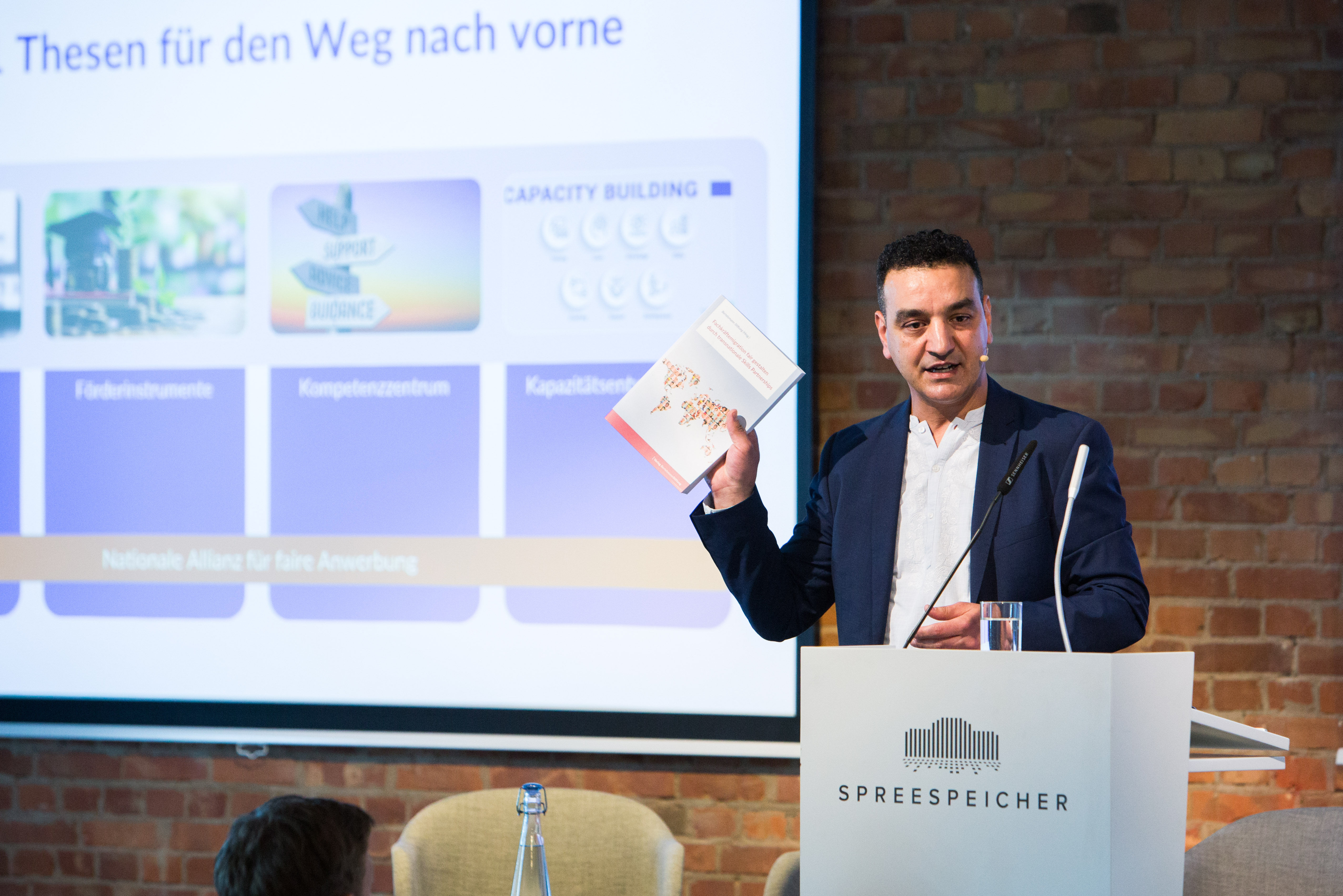 Najim Azahaf von der Bertelsmann Stiftung präsentiert dem Publikum die Abschlusspublikation „Fachkräftemigration fair gestalten durch transnationale Skills Partnerships